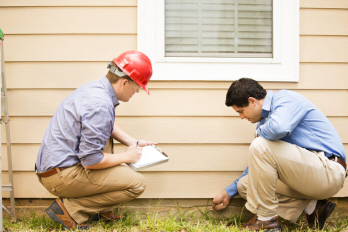 Inspectors or blue collar workers examine building wall, foundation. Outdoors.