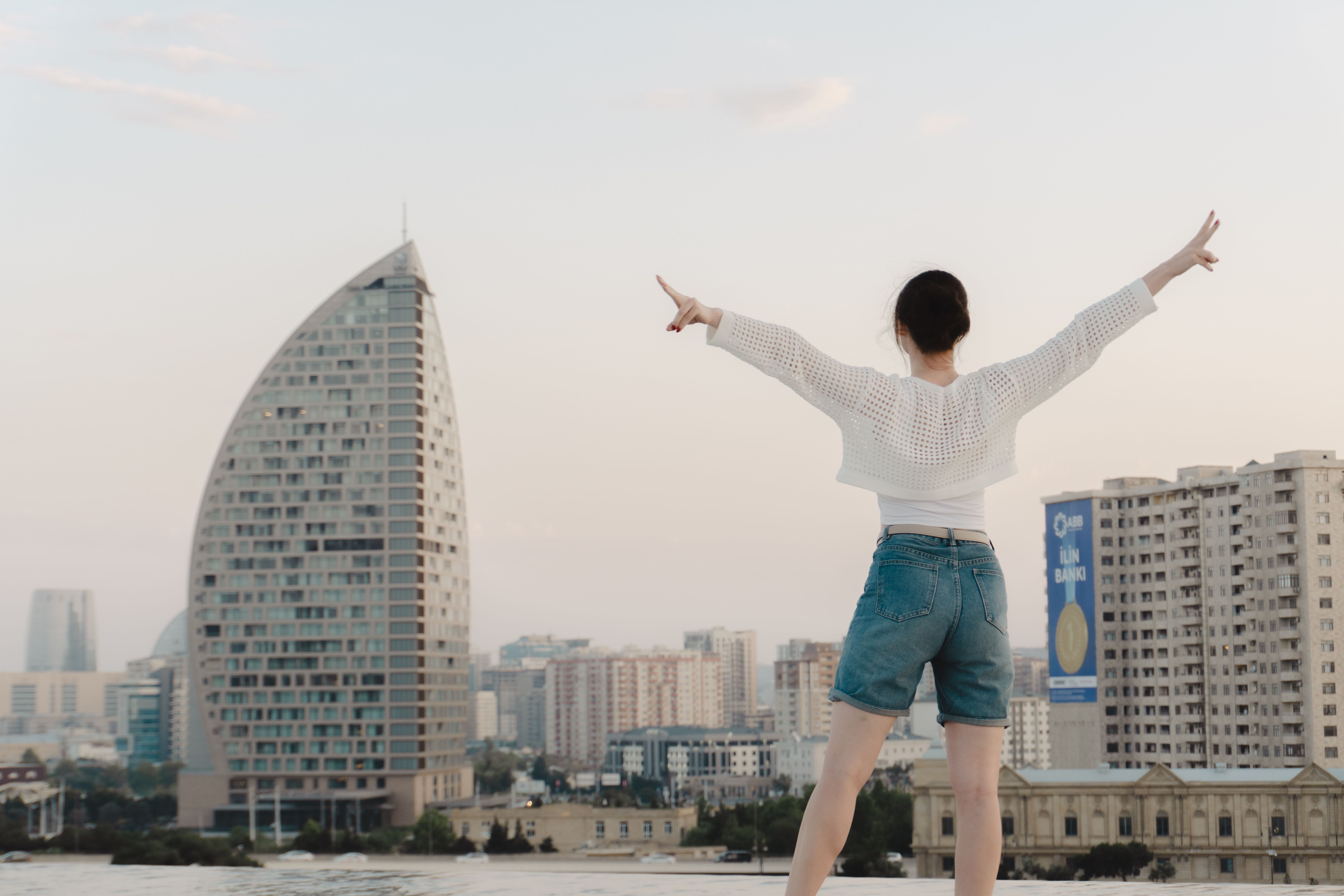 Traveler on a rooftop with arms raised overlooking a modern city skyline at sunset on a weekend adventure